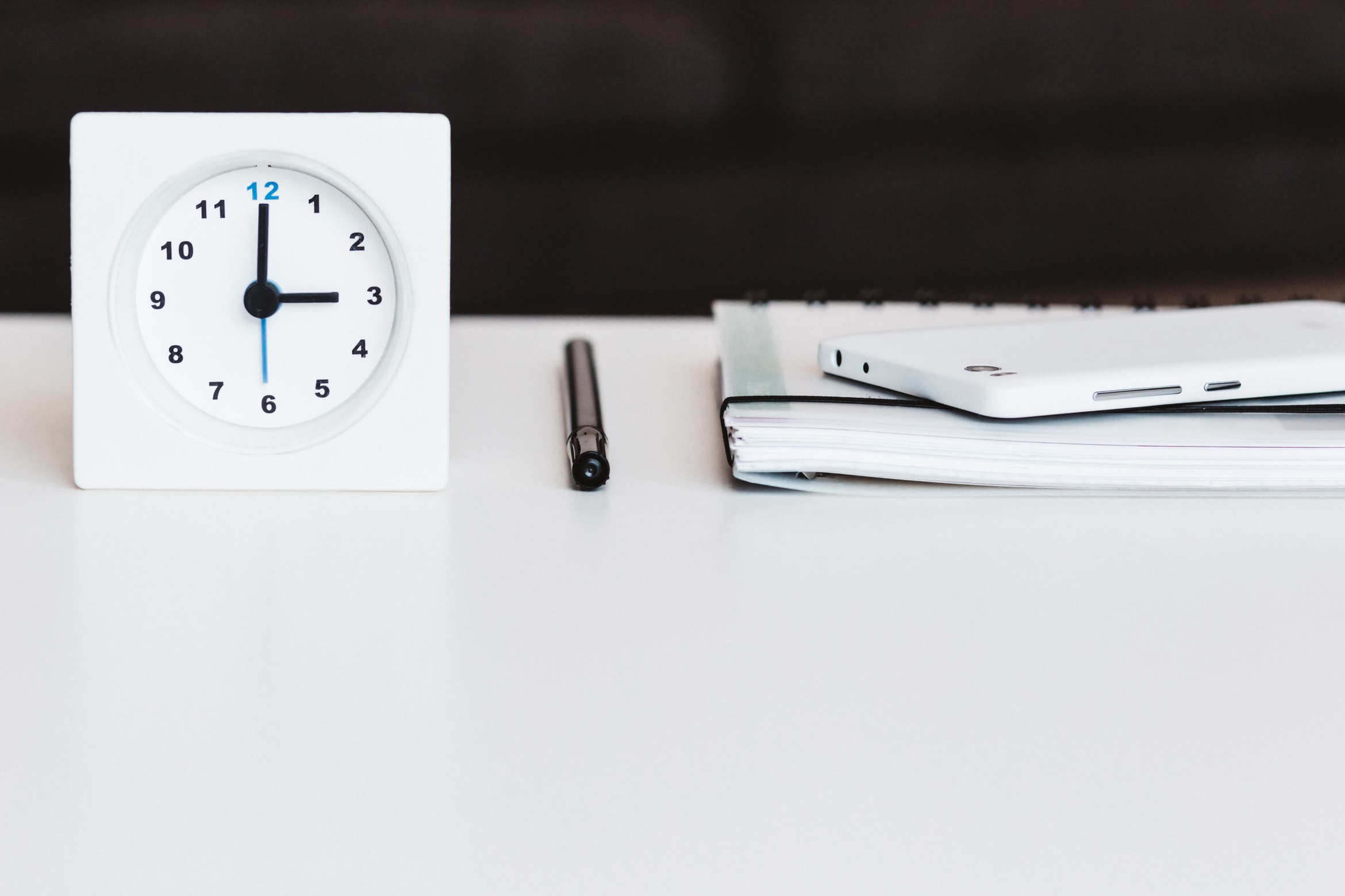 clock sitting on a desk next to a pen and a notebook