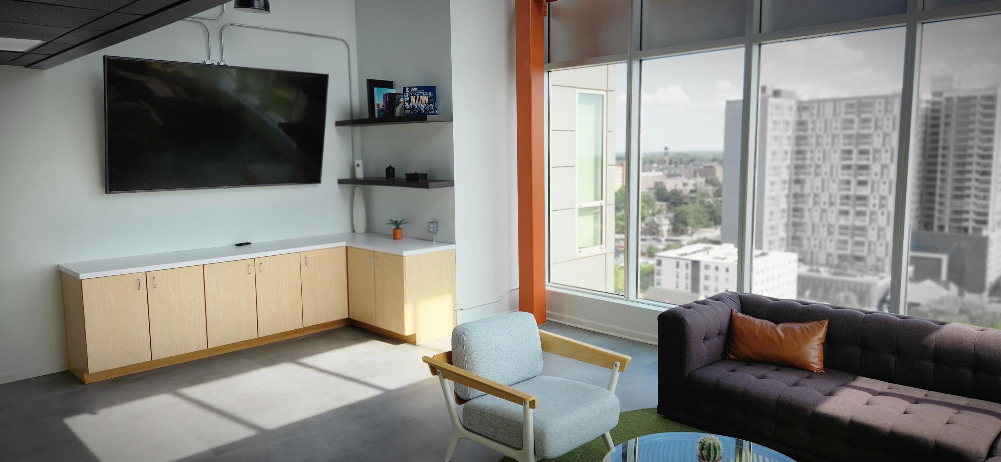 large community room with wall-mounted TV, large windows and modern seating