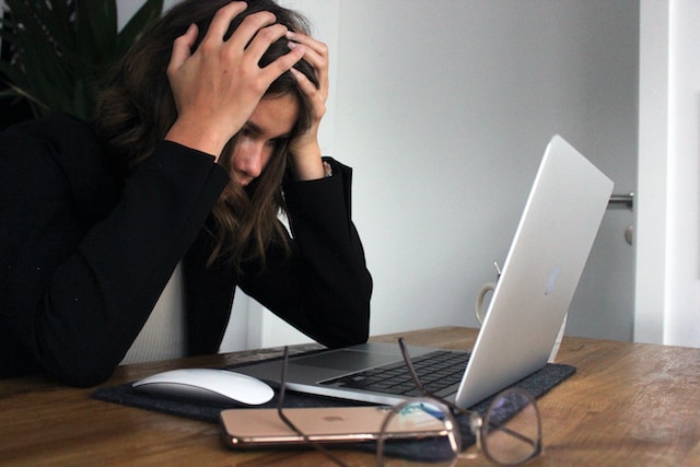 woman in a black long sleeve shirt covering her face with her hands while looking at her laptop